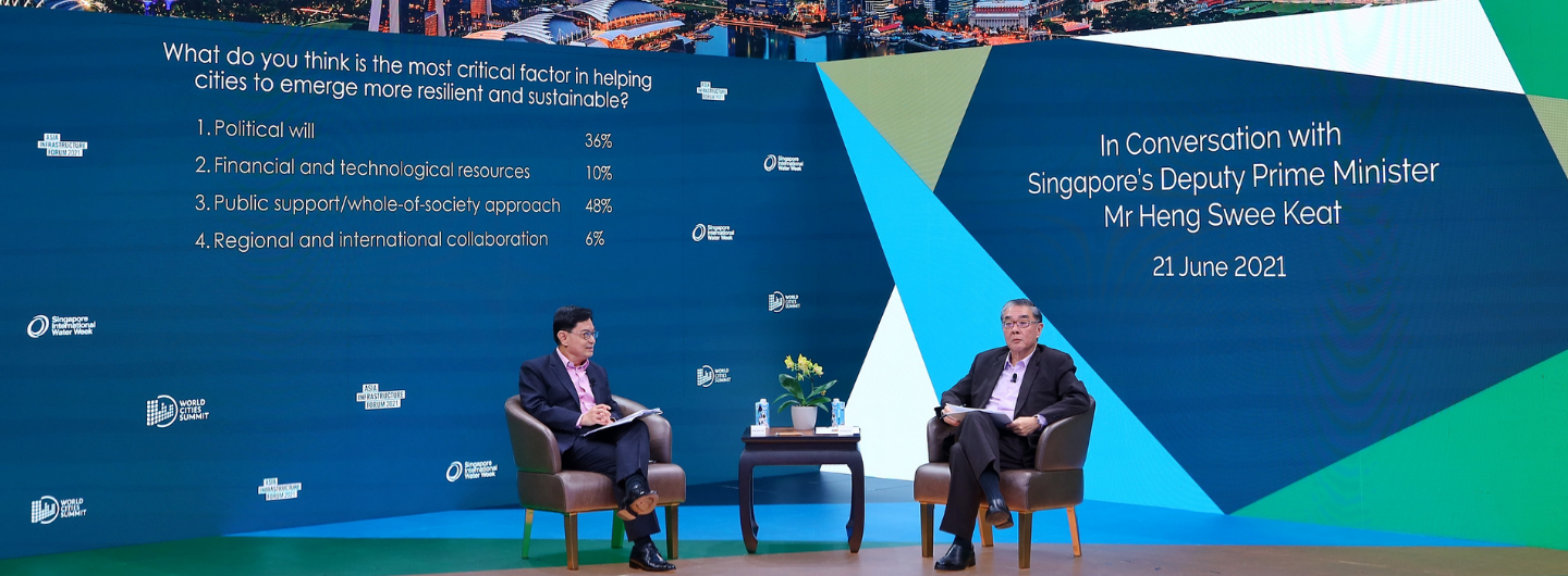 Two men in chairs on stage facing each other; backdrop with city imagery and "Mr Heng Swee Keat".